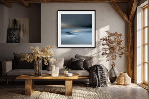 Black-framed Low Tide Light coastal print above a dark sofa in a room with exposed wood beams.