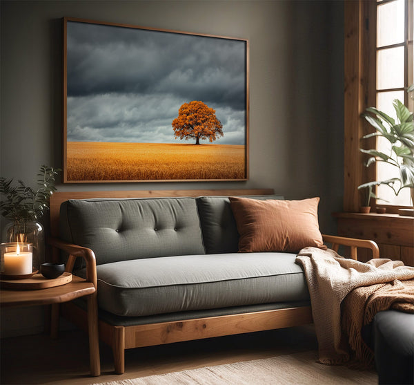 Oak landscape in a slim wood frame above a gray sofa beside a window.