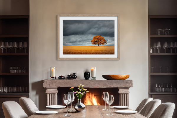 Light wood-framed oak landscape above a lit fireplace and set dining table.