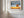 Wood-framed oak landscape print on a white paneled wall beside tall windows.
