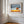 Wood-framed oak landscape print on a white paneled wall beside tall windows.