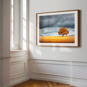 Wood-framed oak landscape print on a white paneled wall beside tall windows.