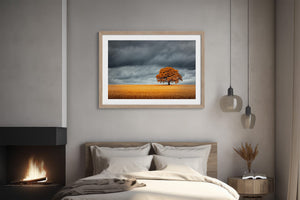 Light wood-framed oak landscape above a bed beside a lit fireplace.