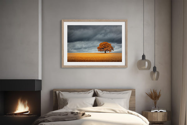 Light wood-framed oak landscape above a bed beside a lit fireplace.