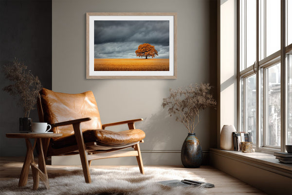 Light wood-framed oak landscape above a leather armchair near large windows.