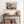 Geometric owl print in a light wood frame above a rustic console table with woven baskets.
