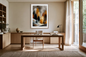 Framed winter tree artwork above a wooden desk in a sunlit neutral-toned workspace.