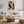 Framed winter tree artwork above a white sofa, rustic coffee table, and woven pouf.