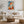 Framed geometric orange fox print above a white sofa, round wood table, and woven ottoman.