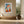 Light wood-framed geometric fox print above a built-in bench beside tall windows.
