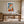 Light wood-framed orange fox print above a wooden desk in a bright workspace.