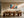 Light wood-framed geometric orange fox artwork above a long wooden dining table and sculptural chairs.