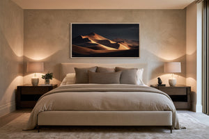 Framed amber sand dunes artwork centered above a bed between two dark wood nightstands.
