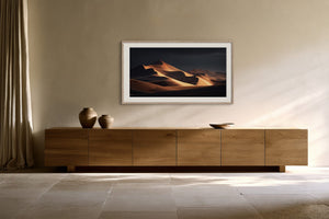 White-framed desert dunes artwork displayed above a long wooden sideboard with ceramic vessels.