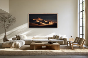 Framed amber dunes artwork hangs above a cream sectional sofa and low wood coffee table.