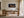 White-framed desert dunes artwork above a wooden desk beside tall windows and sheer curtains.