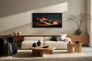 Dark-framed dunes artwork above a cream sofa, round wood tables, and a large ceramic vase.