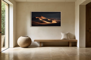 Framed amber dunes artwork above a simple wooden bench in a sunlit tiled entryway.
