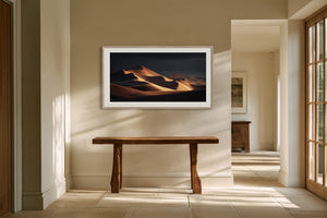 White-framed desert dunes artwork hangs above a rustic wood console table in a bright hallway.