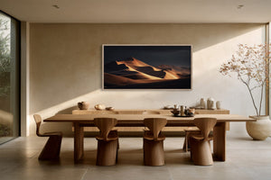 Framed amber sand dunes artwork displayed above a long wooden dining table with sculptural chairs.
