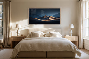 Wide light wood-framed desert dunes artwork above a neatly made bed between bedside lamps.