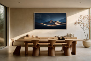 Light wood-framed desert dunes artwork displayed above a long wooden dining table and sculptural chairs.