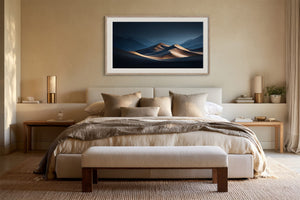 Light wood-framed desert dunes artwork above a bed layered with neutral linens and a bench.