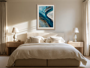Framed teal, navy, grey and gold abstract artwork above a bed between two bedside lamps.