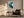 Framed teal and navy abstract artwork above a dark armchair, side table, and floor lamp.