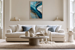 Vertical framed abstract artwork above a white sofa with blue cushions and a round coffee table.