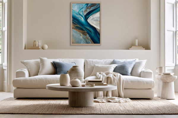 Vertical framed abstract artwork above a white sofa with blue cushions and a round coffee table.