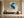 Framed teal, navy and grey abstract artwork above a wooden bench and large round vessel.