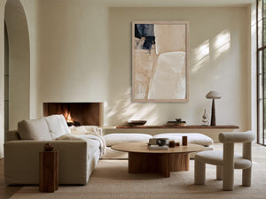 Framed beige and charcoal abstract artwork above a fireplace in a sunlit seating area.