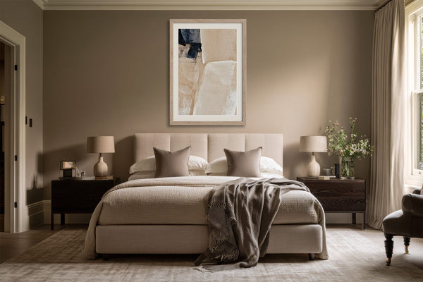 Framed beige and charcoal abstract artwork centered above a bed with dark wood nightstands.