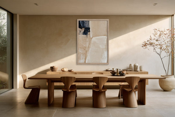 Framed beige and charcoal abstract artwork above a long wooden dining table and sculptural chairs.
