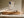 Framed beige and charcoal abstract artwork above a low wooden sideboard in filtered sunlight.