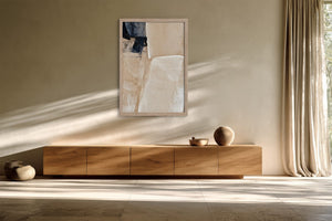 Framed beige and charcoal abstract artwork above a low wooden sideboard in filtered sunlight.