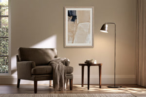 Framed beige and charcoal abstract artwork above an armchair and side table with floor lamp.