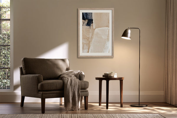 Framed beige and charcoal abstract artwork above an armchair and side table with floor lamp.