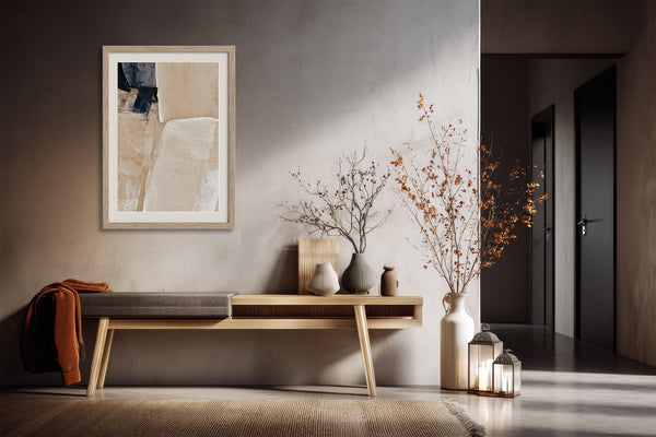 Framed beige and charcoal abstract artwork above a console table with dried branches and lanterns.