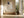 Framed beige and charcoal abstract artwork above a built-in bench beside large windows.