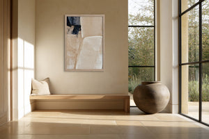 Framed beige and charcoal abstract artwork above a built-in bench beside large windows.