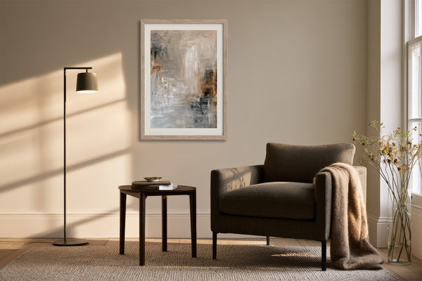 Framed beige, gray, and charcoal abstract artwork above an armchair beside a floor lamp.