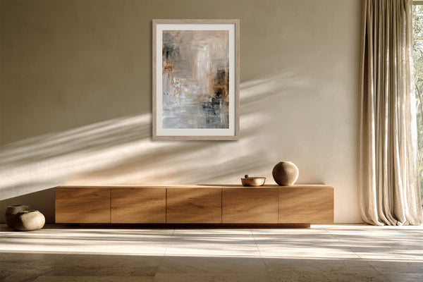 Light-framed layered abstract wall art above a long wooden sideboard in sunlight.