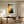 Framed Copper Veil abstract artwork displayed above a wooden desk beside tall curtained windows.