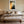 Copper Veil abstract wall art in a pale frame centered above a bed with neutral bedding.