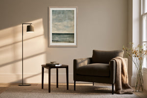 Framed blue-grey abstract artwork above an armchair, side table, and floor lamp.