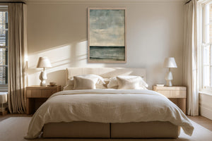 Framed blue-grey abstract artwork centered above a bed between two bedside lamps.