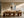 Framed abstract artwork displayed above a long wooden dining table and sculptural chairs.