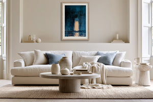 Framed blue abstract artwork with a pale arch hangs above a cream sofa.